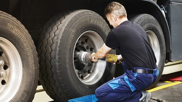 A person kneeling down and screwing the nuts off a  trailer wheel